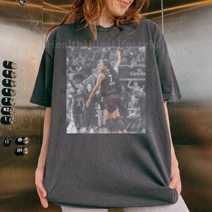 May include: Dark gray t-shirt featuring a black and white image of a basketball player in action. The player is wearing a jersey with the number 7. The text "HealthHuesLifestyle" is printed on the shirt.