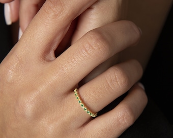 Puede incluir: Un anillo de banda de oro con una fila de pequeñas piedras preciosas de color verde esmeralda.