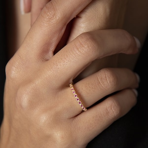 Puede incluir: Un anillo de banda de oro con una fila de pequeñas piedras preciosas rojas.