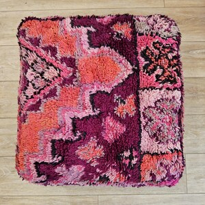 Peut inclure: Un pouf carré et moelleux dans les tons de rose, fuchsia et corail. La surface texturée présente des motifs géométriques et floraux avec des accents noirs. Le pouf est une pièce décorative.