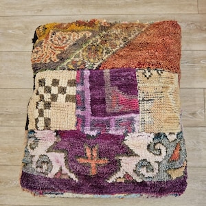 Peut inclure: Un pouf patchwork aux couleurs et textures variées. Le dessus présente des sections orange, jaune et verte. La section du milieu comporte des carrés violets et beiges. Le bas a une bordure violette avec un motif floral.