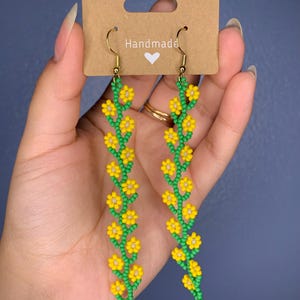 May include: Handmade dangle earrings with a long chain of yellow flowers and green leaves.