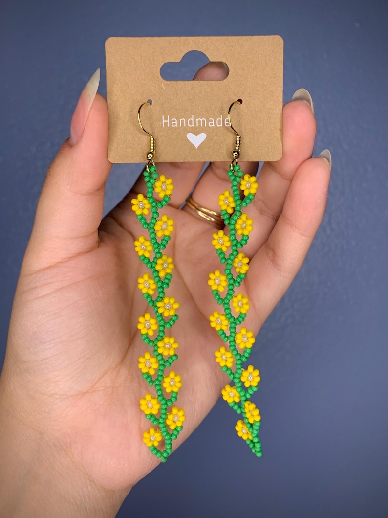 May include: Handmade dangle earrings with a long chain of yellow flowers and green leaves.