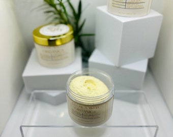Op de afbeelding: Drie potten Glow Naked Organics huidverzorgingsproducten. Twee potten hebben gouden deksels en etiketten, één is open en onthult een gele crème. De potten staan op witte platforms met groen op de achtergrond.
