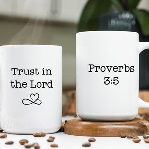 May include: Two white ceramic mugs with black text. One mug says "Trust in the Lord" with an infinity symbol and two hearts. The other mug says "Proverbs 3:5".