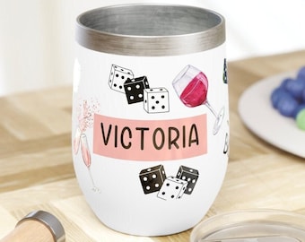 Puede incluir: Un vaso de vino de acero inoxidable blanco con un diseño rosa y negro con dados, copas de vino y el nombre "VICTORIA".