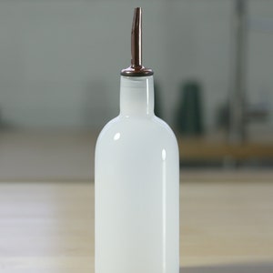 May include: A white glass bottle with a copper spout. The bottle is sitting on a wooden surface.