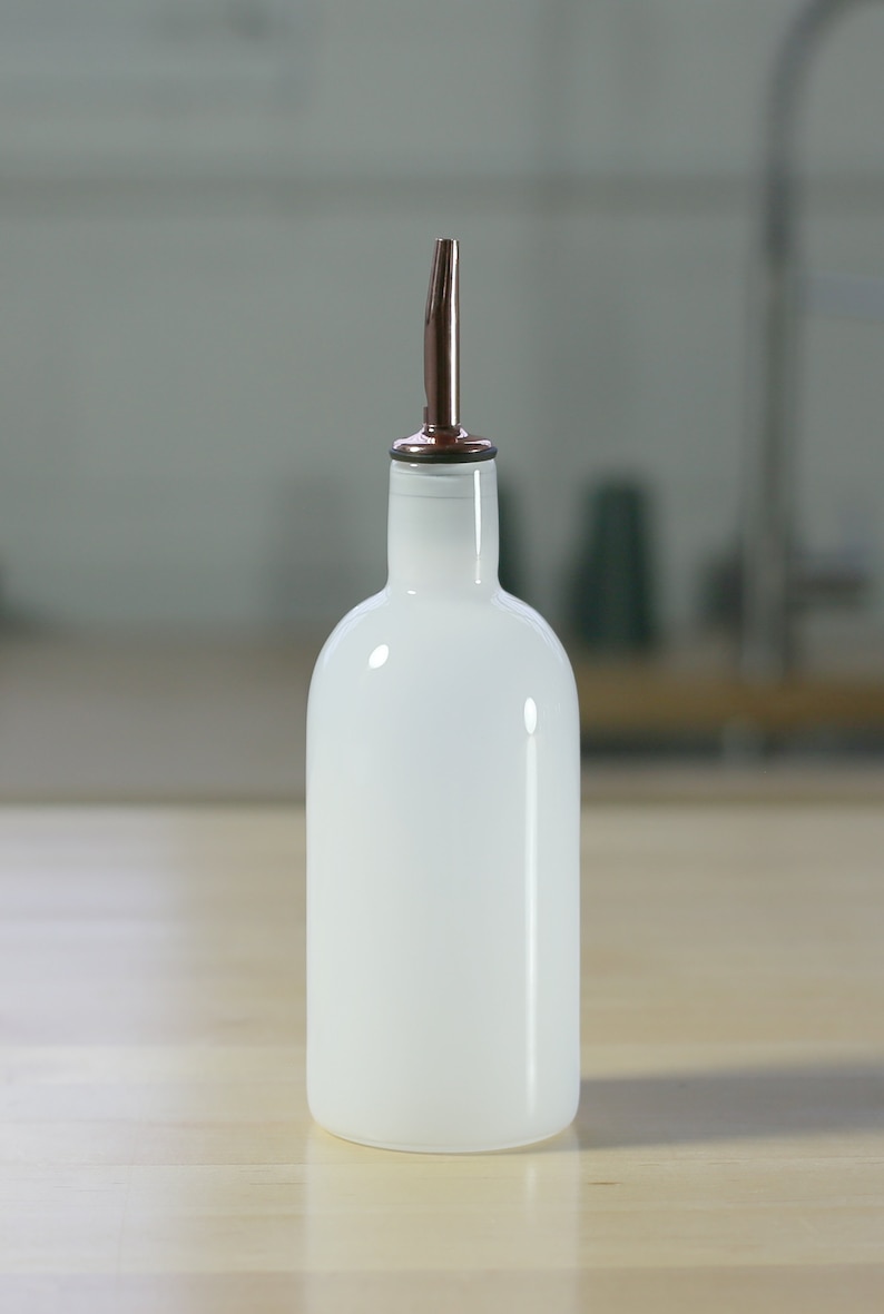 May include: A white glass bottle with a copper spout. The bottle is sitting on a wooden surface.
