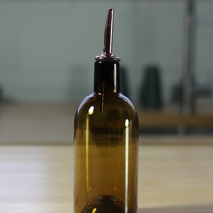 May include: A brown glass bottle with a copper pour spout. The bottle is sitting on a light wood surface.
