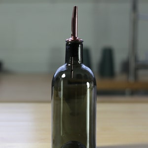 May include: A dark brown glass bottle with a copper spout. The bottle is designed for dispensing oil or vinegar.