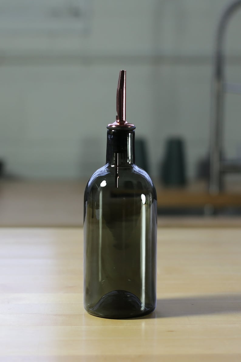 May include: A dark brown glass bottle with a copper spout. The bottle is designed for dispensing oil or vinegar.