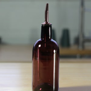 May include: A dark purple glass bottle with a silver spout. The bottle is sitting on a wooden surface.