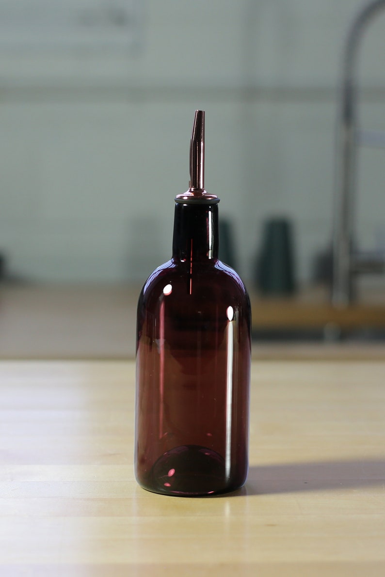May include: A dark purple glass bottle with a silver spout. The bottle is sitting on a wooden surface.
