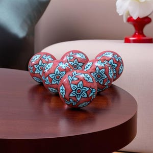 May include: Six decorative spheres with a floral pattern. The spheres are red with blue and white floral designs. The spheres are on a dark wood surface.