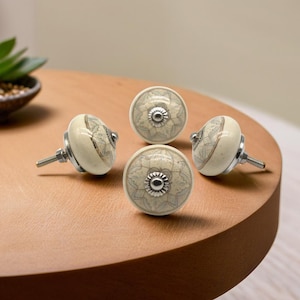 Könnte beinhalten: Vier Keramikknöpfe mit weißem Hintergrund und grauem Blumendesign. Die Knöpfe haben eine silberne Metallbasis und eine Schraube.