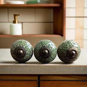 May include: Three green ceramic cabinet knobs with a white and green floral pattern and a metal accent in the centre.