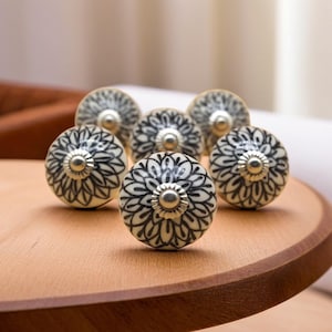 Op de afbeelding: Een set van zes witte keramische ladegrepen met zwarte bloemmotieven en zilveren accenten.