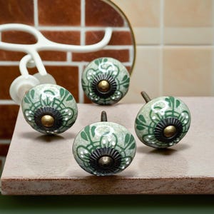 May include: Four ceramic knobs with a green and white floral design. The knobs have a brass screw and a black metal base.