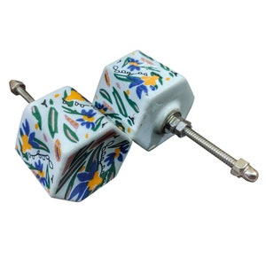 May include: Two white ceramic cabinet knobs with a floral design in blue, yellow, and green. Each hexagonal knob has a metal screw for fitting. These decorative knobs are perfect for updating furniture with a touch of colour and pattern.
