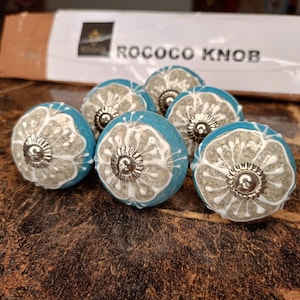 May include: Set of eight ceramic knobs with a white floral design on a blue background. Each knob has a silver metal accent in the center. The knobs are labeled "Rococo Knob".