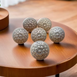 Könnte beinhalten: Sechs graue Keramik-Knöpfe mit floralem Muster. Die Knöpfe sind in einem Kreis auf einer Holzoberfläche angeordnet.