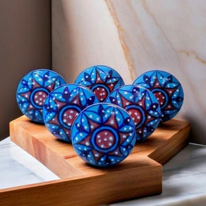 May include: Six blue ceramic knobs with a white and red floral design. The knobs are arranged in a circle on a wooden surface.