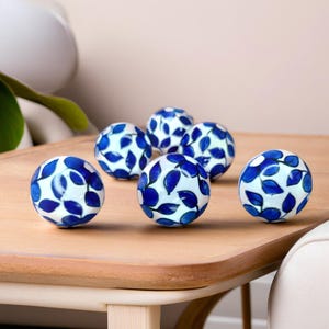 May include: Six blue and white ceramic knobs with a leaf pattern. The knobs are round and have a glossy finish.