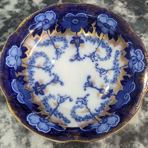 Puede incluir: Un cuenco de porcelana azul y blanco con un borde dorado y un diseño floral. El cuenco tiene un borde festoneado y está decorado con flores y hojas azules y blancas.