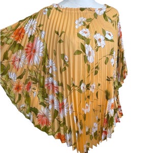 May include: A pleated, yellow top with a floral pattern. The design features white, orange, and pink flowers with green leaves. The top has a round neckline and a flowing, cape-like silhouette.