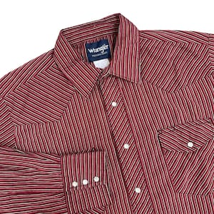 May include: A red and white striped Wrangler Western shirt. The shirt has a button-down front, two chest pockets, and buttoned cuffs. The Wrangler label is visible on the collar.