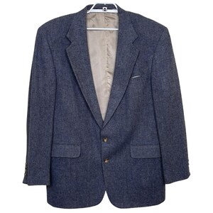 May include: A blue tweed blazer with a two-button closure, notched lapels, and two front pockets. The blazer is hanging on a white hanger against a white background. The interior lining is a light tan color.