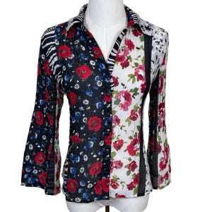Peut inclure: Chemise à boutons avec un design divisé. Un côté présente un fond noir avec des coquelicots rouges et des fleurs bleues, l'autre un fond blanc avec des roses rouges. Les manches sont évasées.