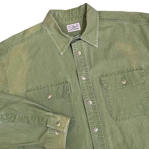Puede incluir: Una camisa verde oliva con botones, dos bolsillos en el pecho y cuello. La camisa tiene un aspecto descolorido y presenta la etiqueta de la marca "LL Bean". La camisa de manga larga tiene puños abotonados.