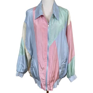 May include: A long-sleeve zip-up jacket featuring a colour-blocked pattern in pastel shades of pink, light blue, mint green, and cream. The garment has a pointed collar, a full-length silver-tone zip, and ribbed cuffs and hem for a structured fit.