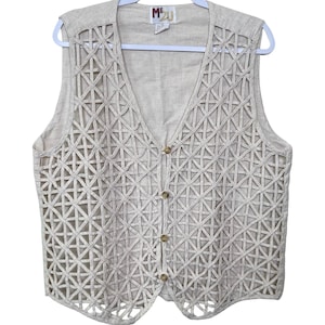 May include: Beige sleeveless vest with a geometric lattice design. The vest has a V-neck, button closure, and a tag that reads "MEJ". The vest is hanging on a white hanger.