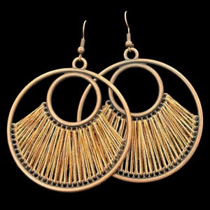 May include: A pair of copper-toned earrings with a circular design. Each earring has a large outer circle, a smaller inner circle, and a fan-shaped fringe of gold threads. The earrings hang from a simple hook.