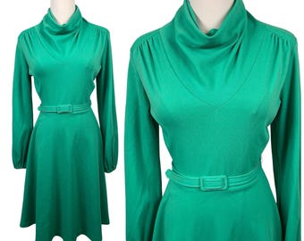 May include: A bright green long-sleeve dress featuring a cowl neckline, a fitted waist with a matching belt, and a flared skirt. The garment has long sleeves with gathered cuffs and a solid, smooth texture throughout the entire piece.