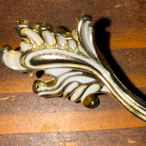May include: A gold and white ornate decorative cabinet pull with a leaf design.