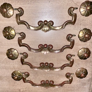 Peut inclure: Ensemble de cinq poignées de tiroir en laiton antique avec des motifs floraux ornés. Chaque poignée est dotée d'un bouton décoratif et d'une poignée incurvée.
