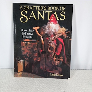 May include: A Crafter's Book of Santas by Leslie Dierks. The book cover is black with gold lettering and features a Santa Claus figure in a red coat and hat, holding a walking stick and a basket. The book promises more than 50 festive projects.