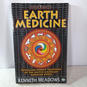 May include: A paperback book titled Earth Medicine by Kenneth Meadows with a black cover featuring a geometric pattern. The center displays a circular graphic with a rainbow spiral and twelve white animal silhouettes representing calendar dates.