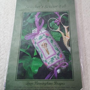 May include: A white ceramic mug with a black handle and the text "But First, Coffee" in a bold, black font. The mug is set against a blurred background, suggesting a cozy setting.