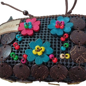 May include: A small, dark mesh purse decorated with wooden flowers in pink, teal, and yellow, and coconut shell accents. The purse has a tag that reads "JAMAICA".