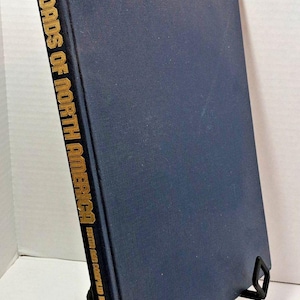 Puede incluir: Un libro de tapa dura de color azul oscuro titulado "Railroads of North America" con letras doradas. El libro está en un soporte de libro negro.
