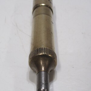 May include: A vintage brass and silver-toned metal object with a cylindrical body. The object has a textured grip and a small, hollow tip. The brass has a slightly aged appearance.