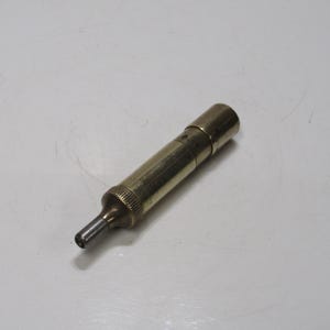 May include: A vintage brass tool with a cylindrical body and a pointed tip. The tool has a textured grip near the tip and a cap on the end. The brass has a warm, aged patina, suggesting it is an antique or vintage item.