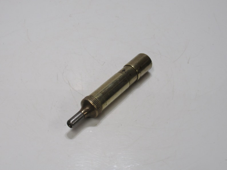 May include: A vintage brass tool with a cylindrical body and a pointed tip. The tool has a textured grip near the tip and a cap on the end. The brass has a warm, aged patina, suggesting it is an antique or vintage item.