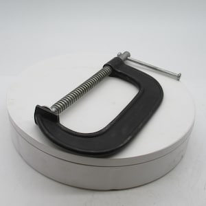 May include: A black C-clamp with a silver threaded rod and handle. The clamp is made of metal and is designed for holding objects together. The C-clamp is a common tool used in woodworking and metalworking projects.