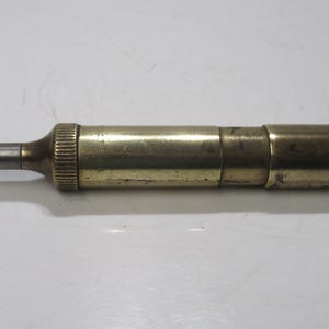 May include: A vintage brass telescope with a silver eyepiece. The cylindrical telescope has a ribbed section near the eyepiece and a smooth, rounded end. The brass has a slightly aged patina, showing its age.