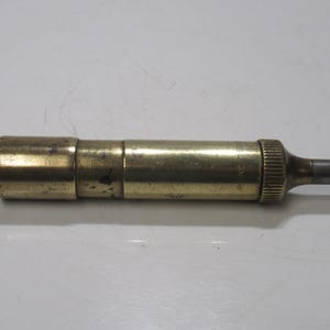 May include: A vintage brass object with a cylindrical body and a small, ridged end. The object has a tarnished, aged appearance, suggesting it is an antique. The end has a small, dark grey, cylindrical tip. The word "Rancaster" is printed on the side.